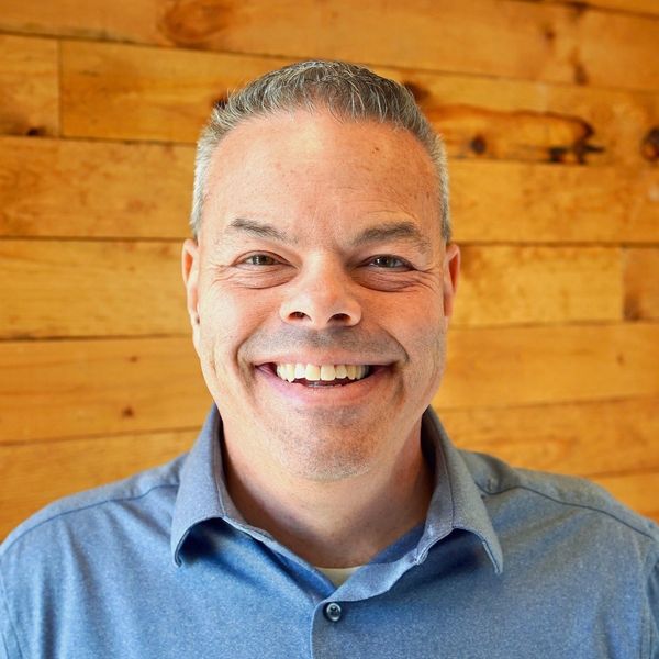 Smiling man in a blue shirt against a wooden background.