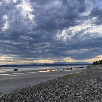 Cloudy sky over a rocky beach with distant mountains and calm water.
