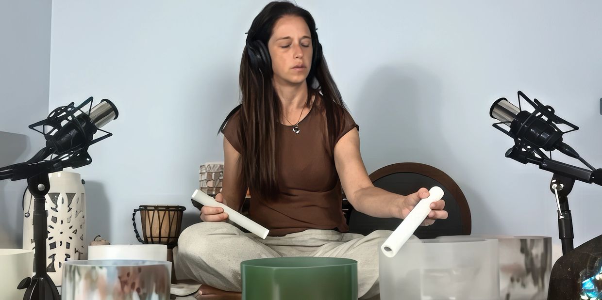 A woman plays crystal singing bowls surrounded by microphones and crystals.
