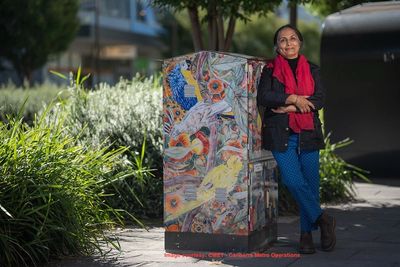 A woman visual artist standing by the metro electric box wrapped up with artwork