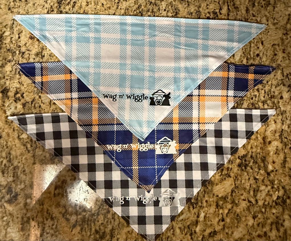 Three plaid dog bandanas in blue, orange, and black patterns laid out on a granite surface.