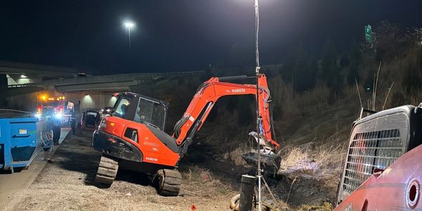 A Kubota excavator working at night on a roadside construction site.