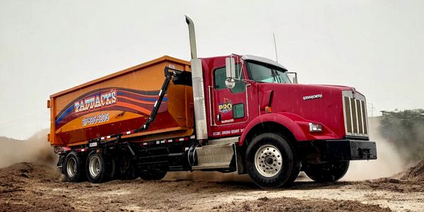 Red Kenworth dump truck unloading dirt at a construction site.