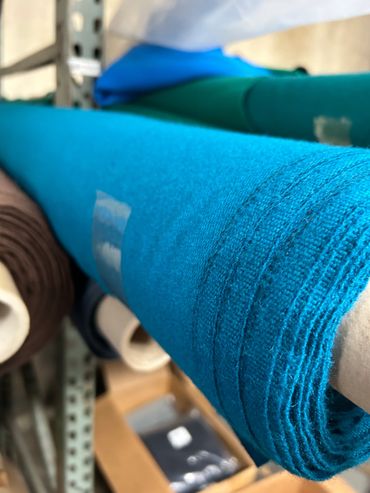 Rolls of vibrant blue and green fabric stored on a shelf in a textile warehouse.