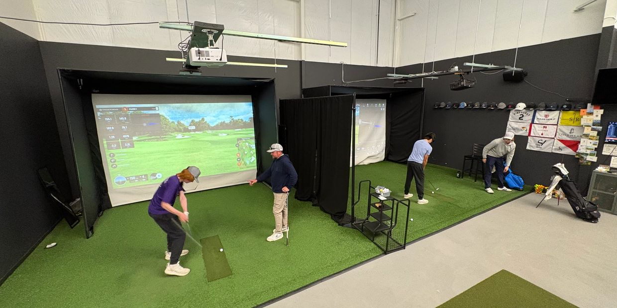 Two indoor golf simulators with players practicing their swings and receiving coaching.