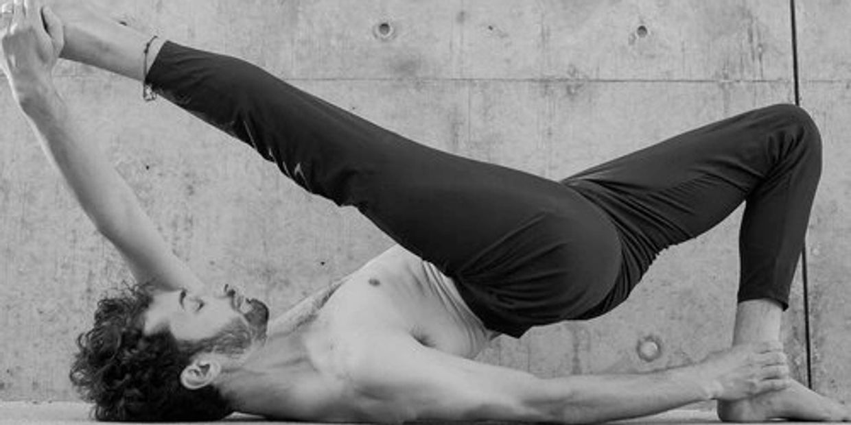 Man practicing advanced yoga pose on floor against concrete wall.
