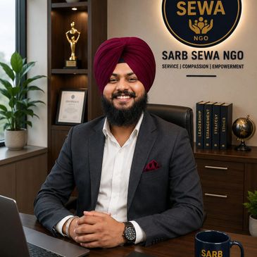 Smiling man in a turban sits at a desk with Sarb Sewa NGO logo behind him.