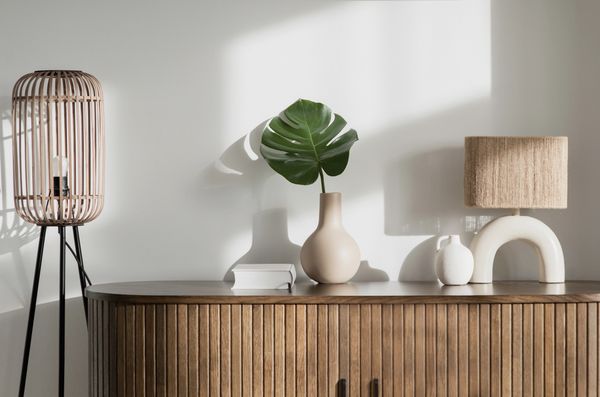 Minimalist decor on wooden sideboard with lamp and green leaf.