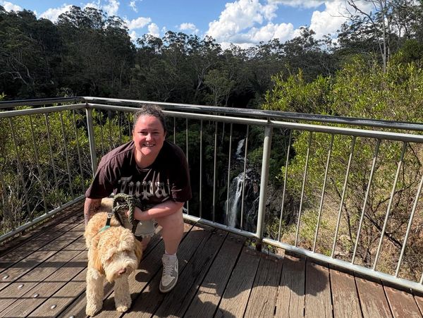 Woman crouching with her dog on a wooden platform near a waterfall.
