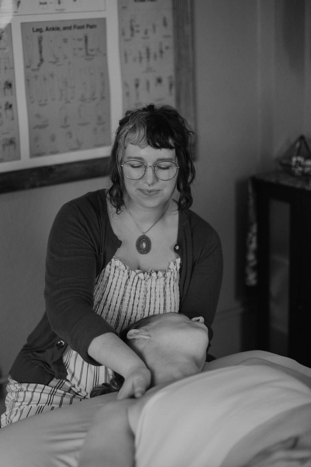 A woman with glasses giving a neck massage to a person lying down.