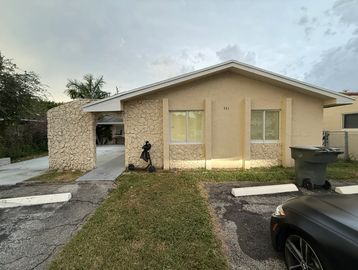 Small beige house with a car parked in front and a driveway.