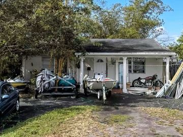 Small house with trailers and motorcycle parked outside.