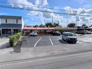 Parking lot with several cars in front of stores under a blue sky.