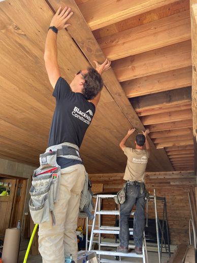 Two construction workers installing wooden panels on a ceiling.