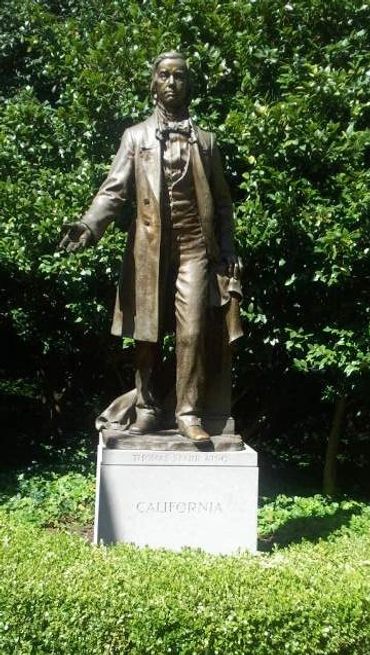 Statue of a man in historical attire labeled California, surrounded by greenery.