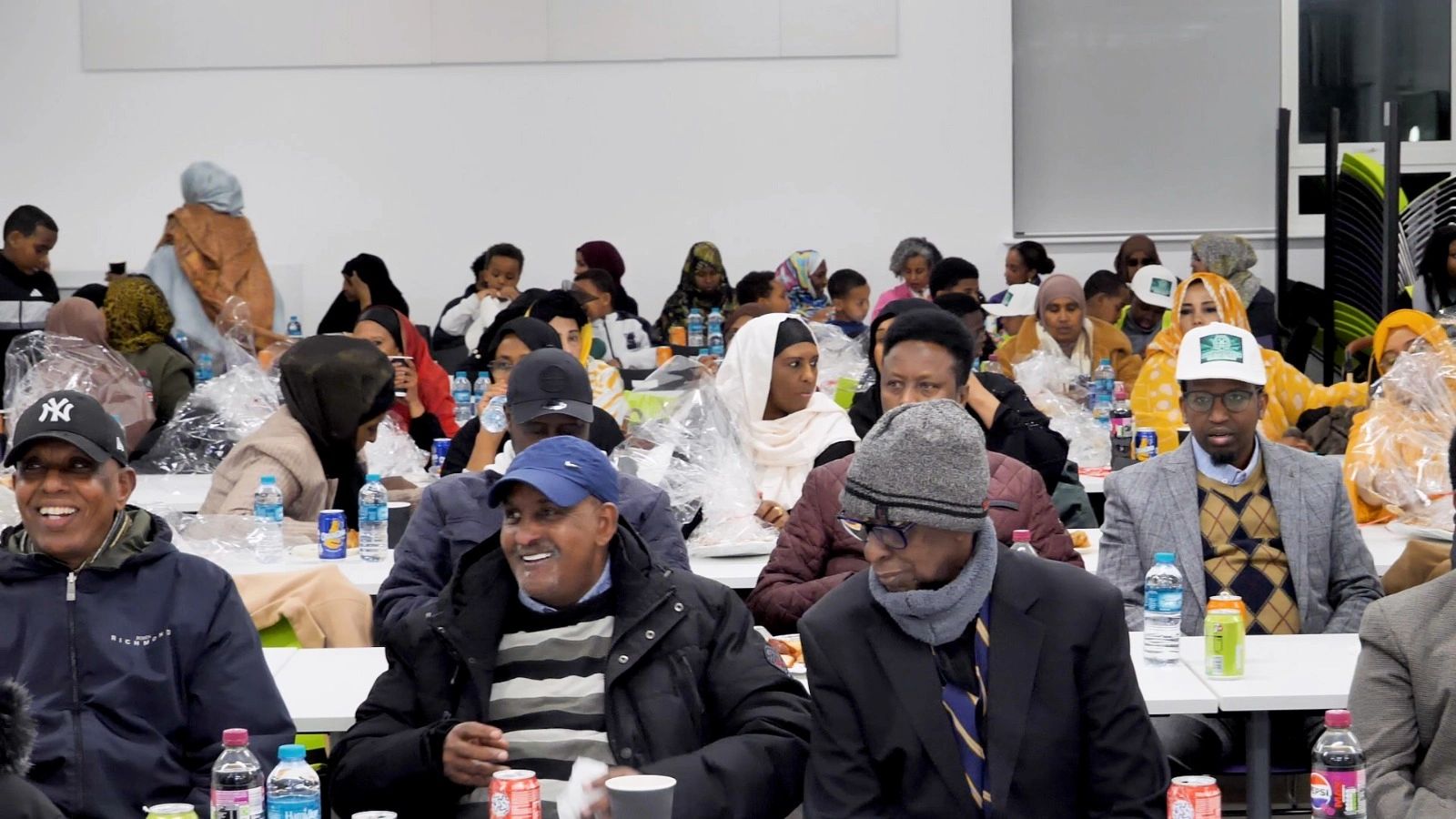 A diverse group of people gathered in a hall, enjoying drinks and socializing.