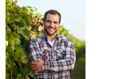 A man in a plaid shirt standing by a grapevine