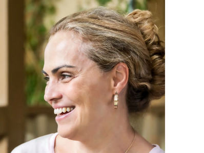 A happy smiling woman, in a sandy blonde updo, gold earrings, looking affectionately to her right