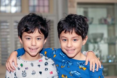 Grinning twin boys with arms around each other's shoulders in pajamas at home