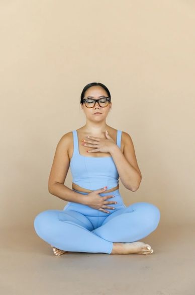 Woman in blue workout clothes meditating with hands on chest and stomach.
