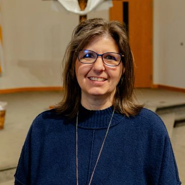 Smiling woman with glasses and a blue sweater indoors.