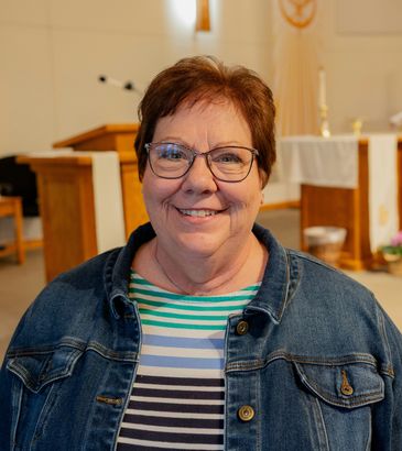 Smiling woman wearing glasses and a denim jacket.