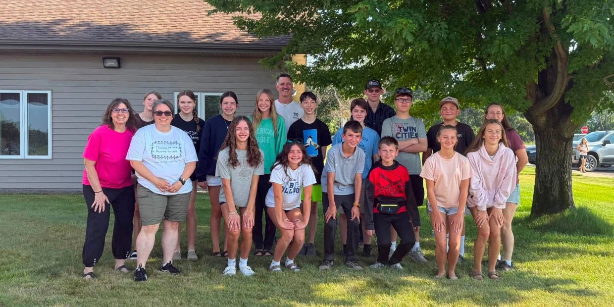 Group of teenagers and adults posing outdoors near a tree and house.