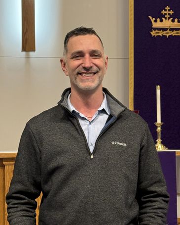 Man smiling inside a church near a cross and candle.