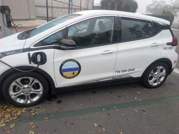 White electric security vehicle charging with Surfside Patrol logo.