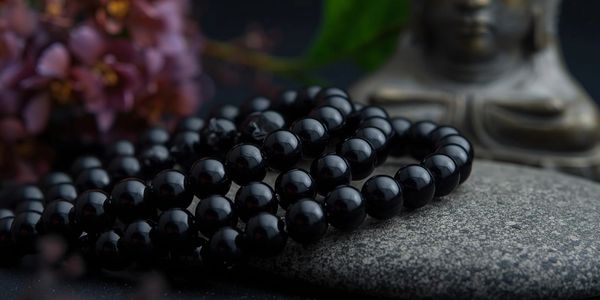 Black bead bracelet on a textured stone with a Buddha statue in the background.