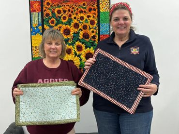 Two women proudly display their handmade quilted placemats.