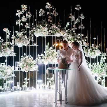 Bride and groom cutting cake amid floral decorations at night.