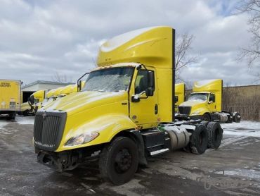 Yellow semi trucks parked outside on a cloudy day.
