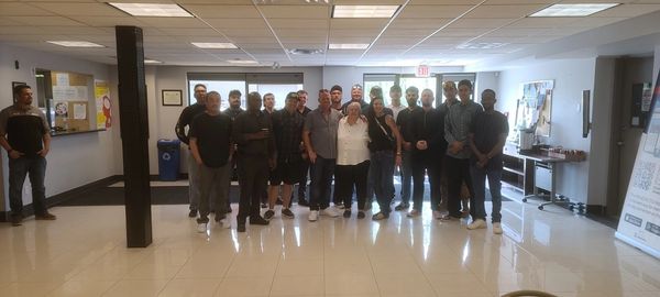 Group of diverse people gathered in a brightly lit indoor space, possibly an office or waiting area.