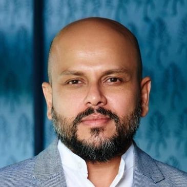 Portrait of a bald man with a beard in a gray suit jacket.