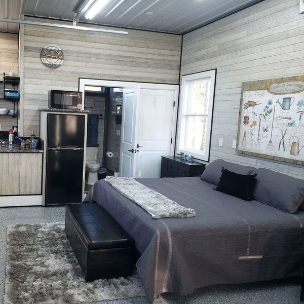 Cozy bedroom with kitchenette and bathroom, featuring neutral tones and soft textures.