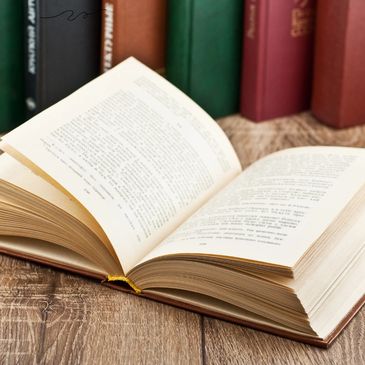 Open book on wooden surface with closed books in the background.