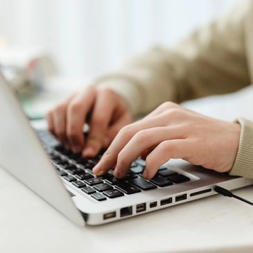 Person typing on a laptop keyboard with focus on hands.
