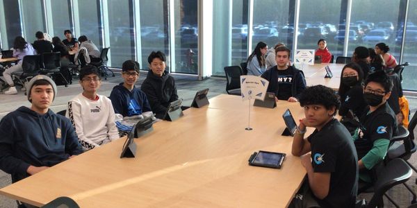 Group of students sitting around a conference table with tablets.