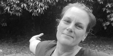 Woman smiling outdoors with arms outstretched in a natural setting.