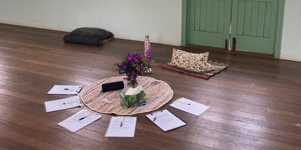 Circle of papers, pens, and cushions around a floral centerpiece on wooden floor.
