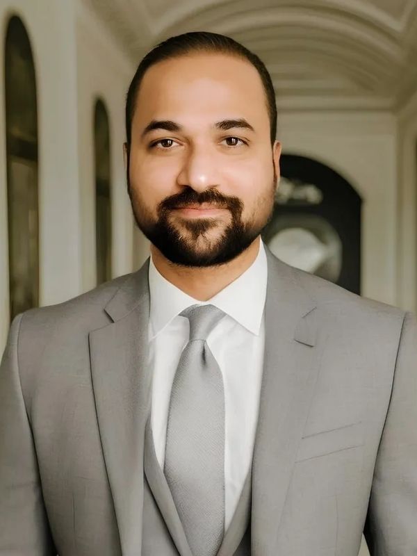 Man in a light gray suit and tie smiling at the camera.