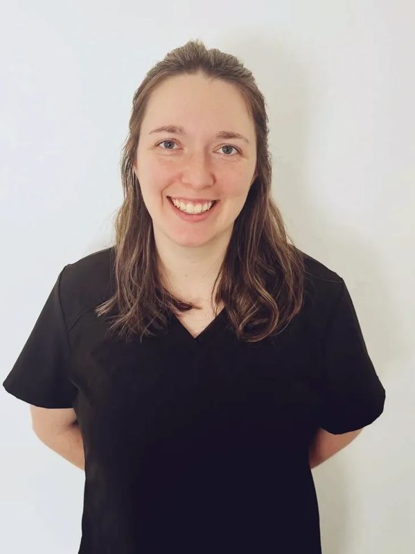 Smiling woman in black medical scrubs stands against a white wall.