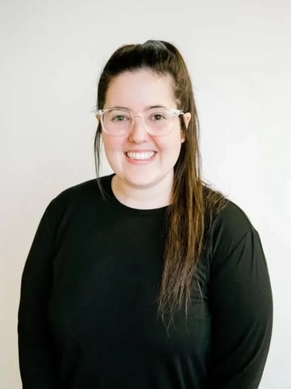 Smiling woman with glasses and a ponytail wearing a black sweater.