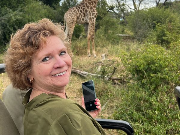 Woman taking a photo of a giraffe in a natural setting.