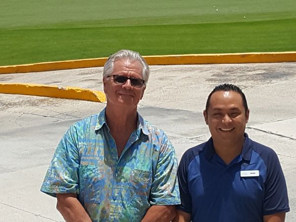 Two men smiling outdoors with a golf course in the background.