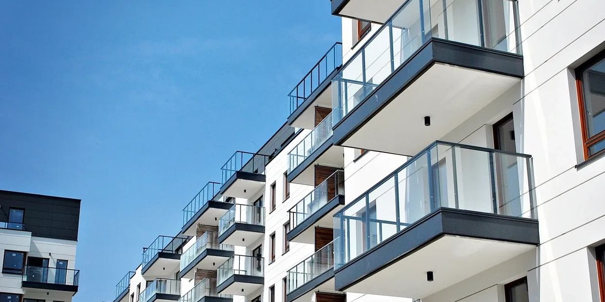 Modern apartment building with glass balconies against clear blue sky.