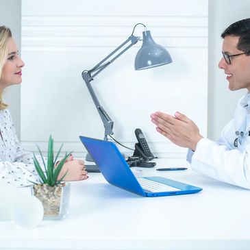 Doctor consulting a patient in a bright office with a laptop.