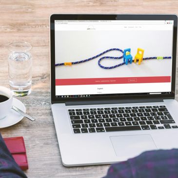 Laptop on a wooden table showing a website with colorful toy chairs and rope.