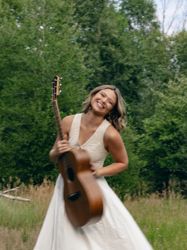 Woman in white dress holding a guitar outdoors.